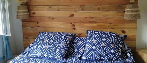 Een slaapkamer met een houten hoofdbord, een bed met blauw beddengoed met een patroon, een lijst met een afbeelding en twee wandlampen.