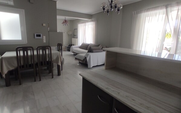 Una habitación moderna y luminosa con una mesa de comedor, sillas, un sofá y un ventanal con cortinas traslúcidas.