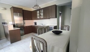 Kitchen features a central island with a bowl, surrounded by cabinets and a refrigerator, sink, stove, and dining table with chairs.