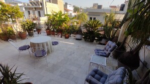 Eine Dachterrasse mit einem runden Tisch und Stühlen, umgeben von Blumentöpfen und Blick auf die Stadt.