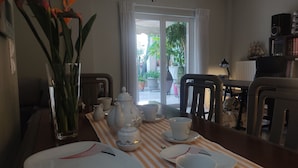 Ein Essbereich mit einem für Tee gedecktem Tisch, mit einer Streifen Tischdecke, weißen Tellern und einer Vase mit Blumen.