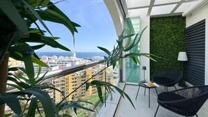 A balcony with a view of the city, a green wall, and two black chairs. - ONE7 Suite – The sunrise penthouse (Estepona)