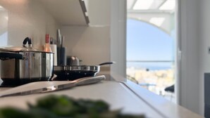A kitchen with a stove, pots, and a view of the city through a window. - ONE7 Suite – The sunrise penthouse (Estepona)