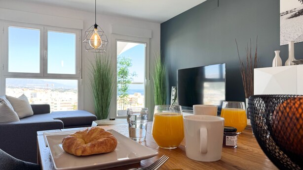 A modern living room with a sofa, a dining table with breakfast items, and a TV. - ONE7 Suite – The sunrise penthouse (Estepona)