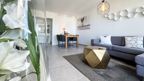 A modern living room with a grey sofa, a wooden coffee table, and a dining area with a wooden table and chairs. - ONE7 Suite – The sunrise penthouse (Estepona)