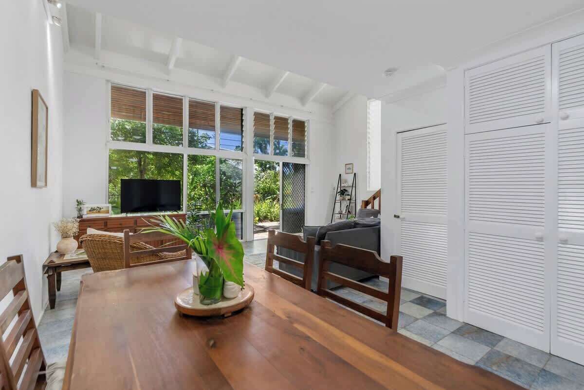 A spacious room with a wooden dining table, a television, and a large window with blinds.