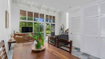 A spacious room with a wooden dining table, a television, and a large window with blinds.