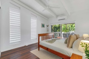 A bedroom with a wooden bed, white walls, a ceiling fan, and a balcony with outdoor furniture.
