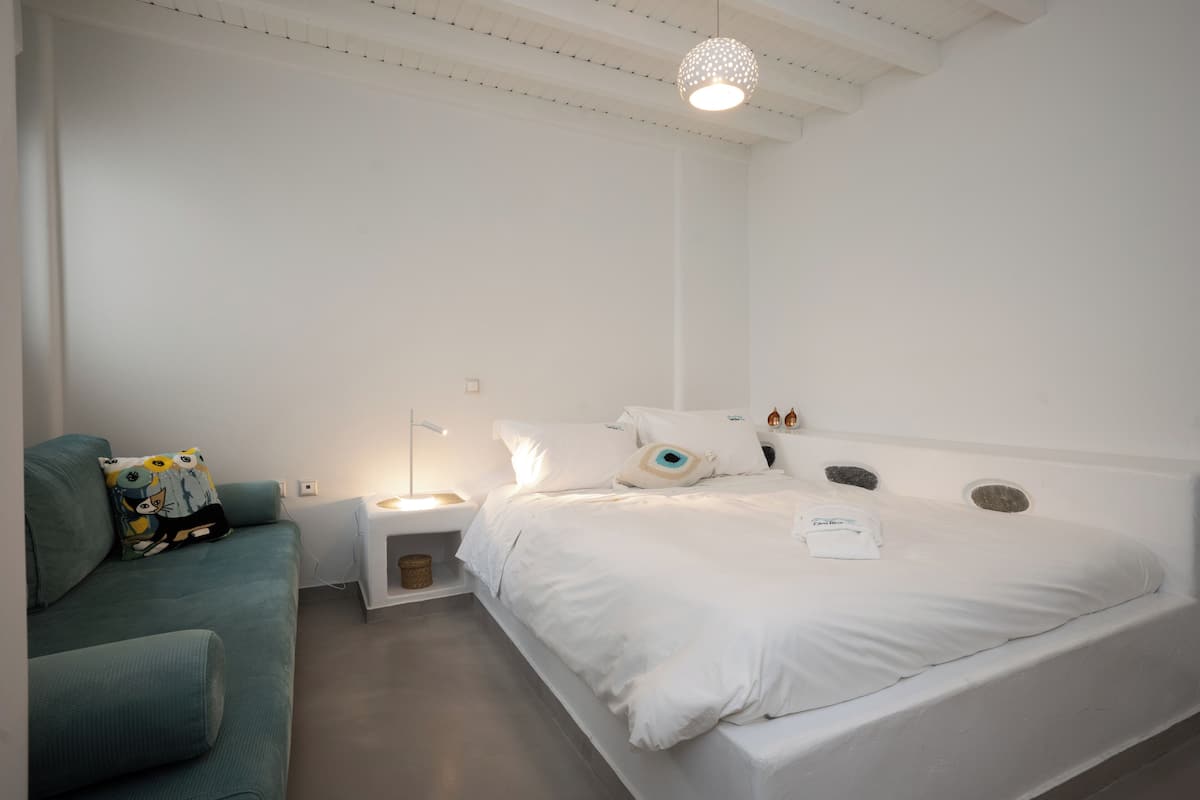 A modern bedroom with a large bed, a bedside table, a lamp, and a sofa with decorative pillows.