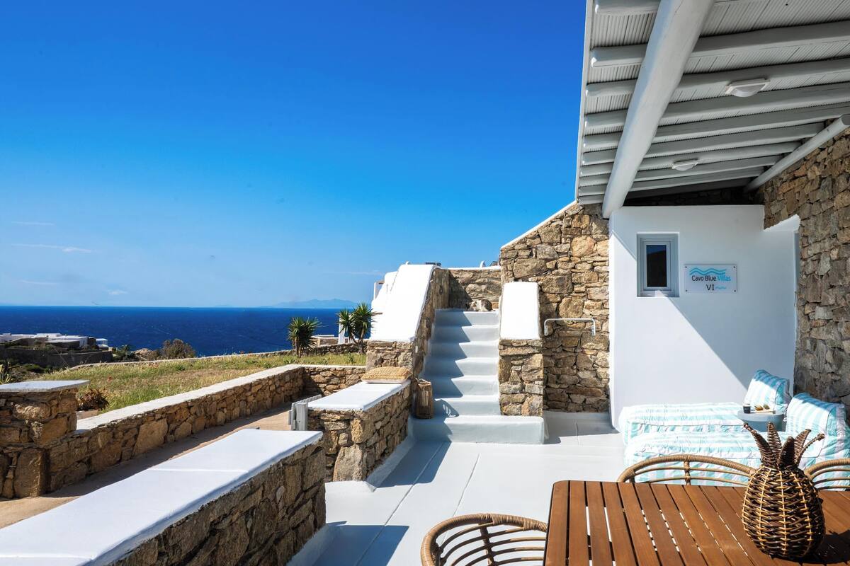A stone building with a staircase leading to a white room with a view of the sea.