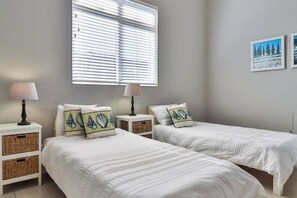 A room with two beds, each with a lamp and a basket.