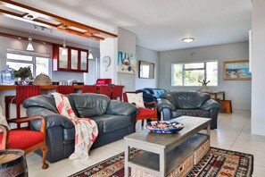 A living room with a sofa, chairs, a coffee table, and a kitchen area in the background.