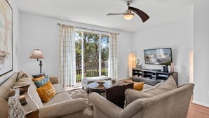 A living room with a sofa, armchairs, a coffee table, a TV, and a ceiling fan. - Comfortable 3BR Near Convention Center Epic Park (Orlando)