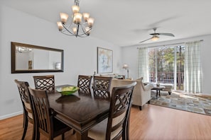A dining room with a wooden table and chairs, a chandelier, a ceiling fan, and a large window with curtains. - Comfortable 3BR Near Convention Center Epic Park (Orlando)
