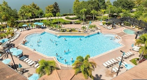 Una gran piscina al aire libre rodeada de sillones de playa y sombrillas, con un jardín ajardinado y vistas a un lago.