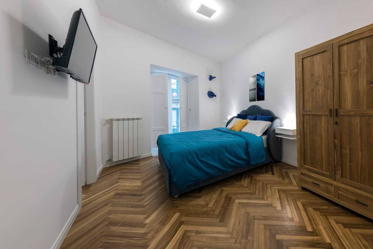 Un dormitorio con cama, armario de madera, radiador y televisor montado en la pared.