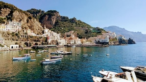 A coastal town with buildings on a hillside, a bridge, and boats in the water. - L'Incanto House (Salerno)