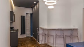 A modern kitchen with a herringbone wood floor, a dining area with clear plastic chairs, and a ceiling light fixture. - L'Incanto House (Salerno)