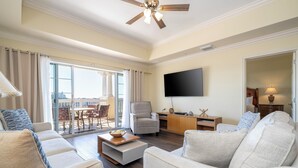 Ein geräumiges Wohnzimmer mit großem Flachbildfernseher, Deckenventilator und einem Balkon mit Essbereich.