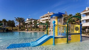 Ein Wasserpark mit einer blauen und gelben Rutsche, einer Fontäne und einem Rettungsschwimmer-Warnschild.