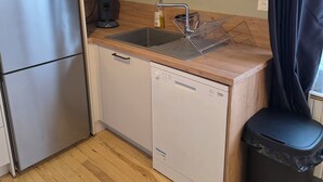 Eine kleine Küche mit Kühlschrank, Geschirrspüler, Spüle und einem kleinen Mülleimer.