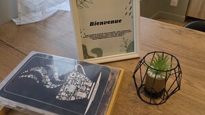 Ein gerahmtes Willkommen-Schild, ein Buch zum Thema Kaffee und ein kleiner Topfpflanze auf einem Holztisch.