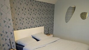 Ein Schlafzimmer mit Bett, Nachttisch und einer Wand mit geometrischem Wandpapier.