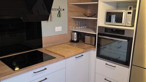 Eine moderne Küche mit weißen Schränken, einer schwarzen Induktionskochplatte, einer Holz Arbeitsplatte, einem Einbauofen, einer Mikrowelle und einer Pendelleuchte.