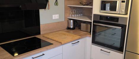 A modern kitchen with white cabinets, a black induction cooktop, a wooden countertop, a built-in oven, a microwave, and a hanging light fixture.