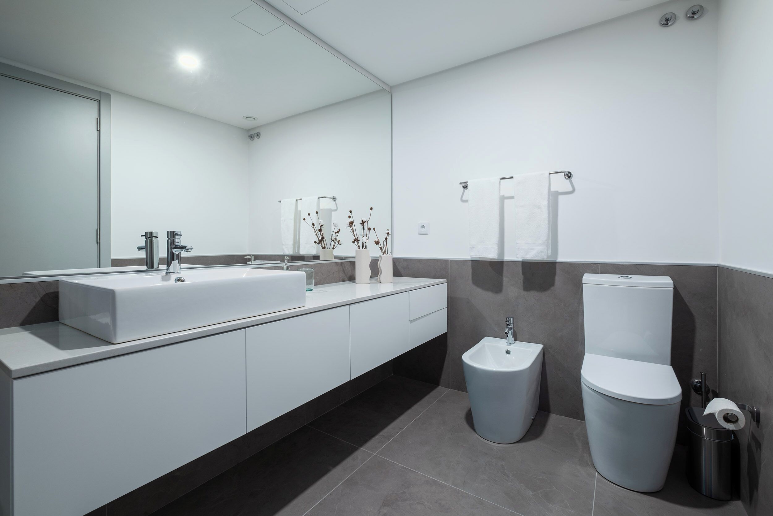 Et moderne badeværelse med en stor hvid vask, en bidét og et toilet.