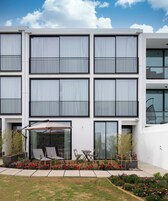 Un edificio moderno con varios balcones, amplias ventanas y un patio con muebles de exterior.
