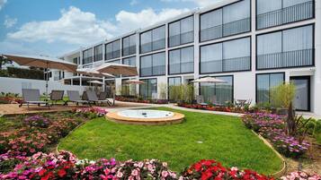 A modern building with a courtyard featuring a hot tub, outdoor seating, and flower beds.