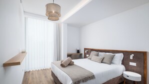 A modern bedroom with a large bed, wooden floor, a bedside table, and a hanging light fixture.