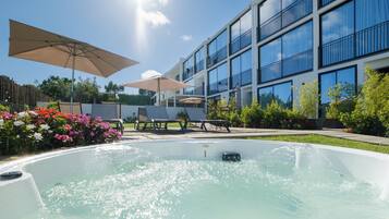 A swimming pool with a hot tub, surrounded by outdoor seating and a modern building with balconies.