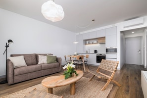 A modern living room with a sofa, coffee table, and a dining area with chairs and a table. - Mónaco Suites & Garden (Ponta Delgada)