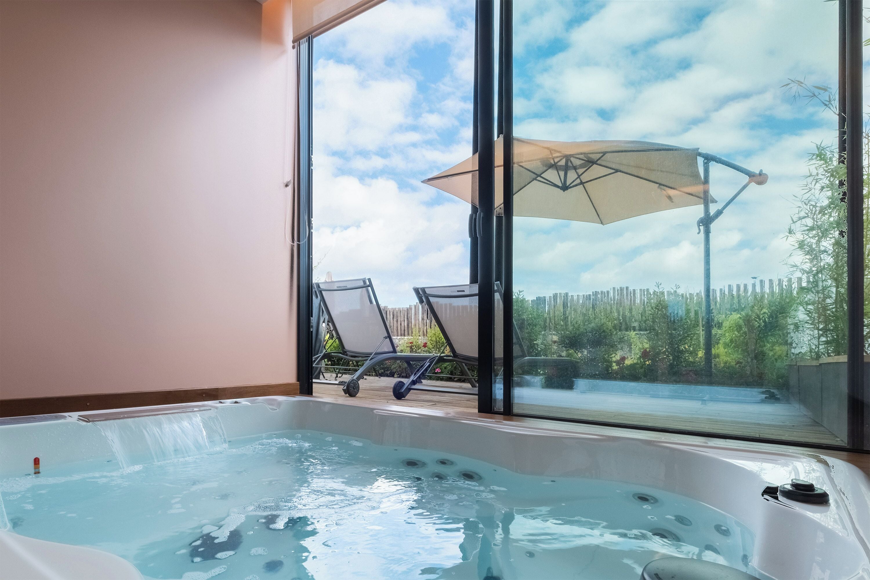 Un bain à remous avec vue sur une terrasse en bois, des chaises, un grand parasol et un ciel dégagé.
