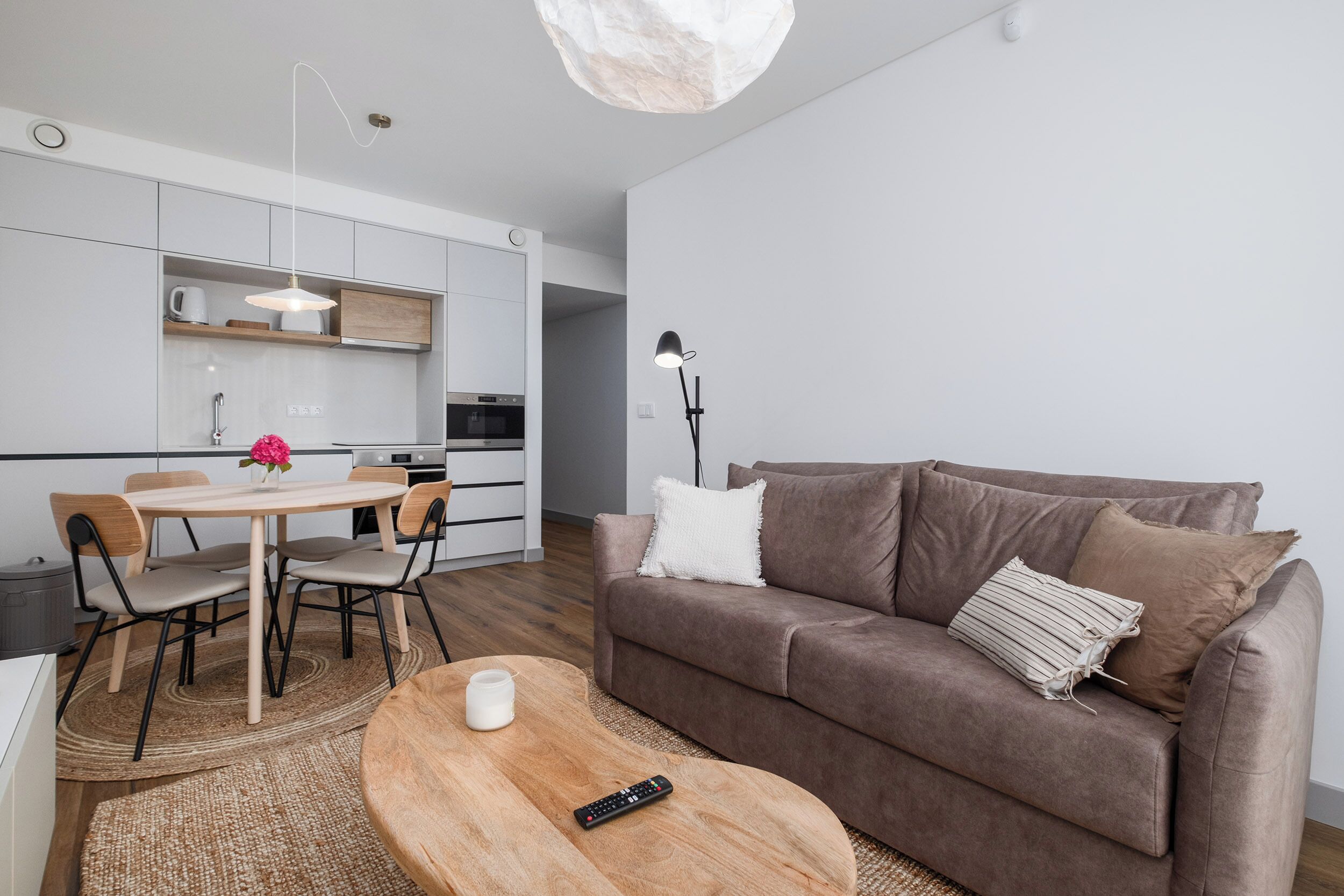 A modern living room with a brown sofa, a wooden coffee table, and a dining area with a round table and chairs.