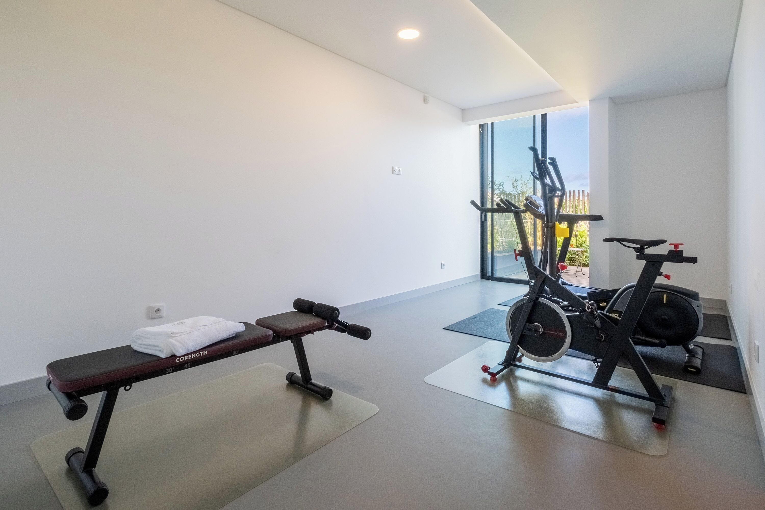 Een sportschool met een bankje, halters en een hometrainer.