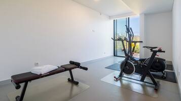 Een sportschool met een bankje, halters en een hometrainer.