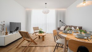 A modern living room with a flat-screen TV, a dining table set with bowls and cups, and a sofa with cushions.