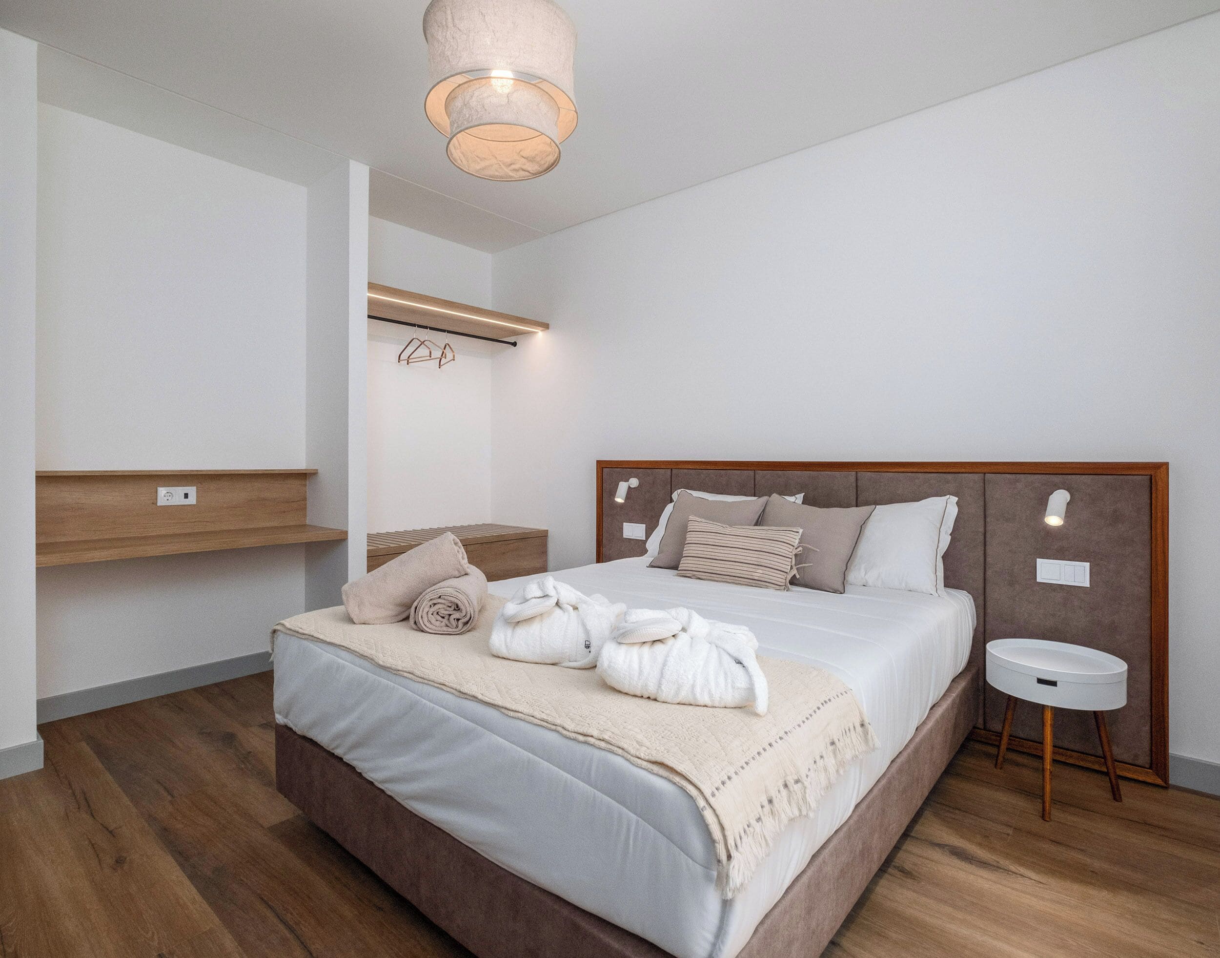 A modern bedroom with a large bed, bedside tables, a hanging light fixture, and a built-in shelf.
