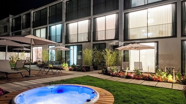 A modern building with a hot tub in the backyard, surrounded by outdoor seating and plants.
