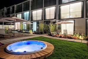 A modern building with large windows, a hot tub, and outdoor seating with umbrellas. - Mónaco Suites & Garden (Ponta Delgada)