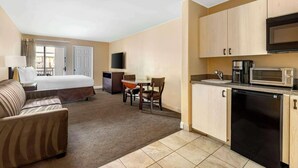 A hotel room with a bed, a sofa, a desk with a chair, a flat-screen TV, a kitchenette with a microwave, coffee maker, and dishwasher. - Hilton Vacation Club Palm Canyon (Palm Springs)