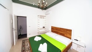 A bedroom with a wooden headboard, a green bedspread, a chandelier, a wardrobe, and a bedside table with a lamp. - Visitsicilia Donn'Anna 3 (Castellammare del Golfo)