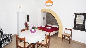 A compact room with a bed, a dining table with chairs, a small table with a vase of flowers, and a hanging light fixture. - Visitsicilia Donn'Anna 1 (Castellammare del Golfo)