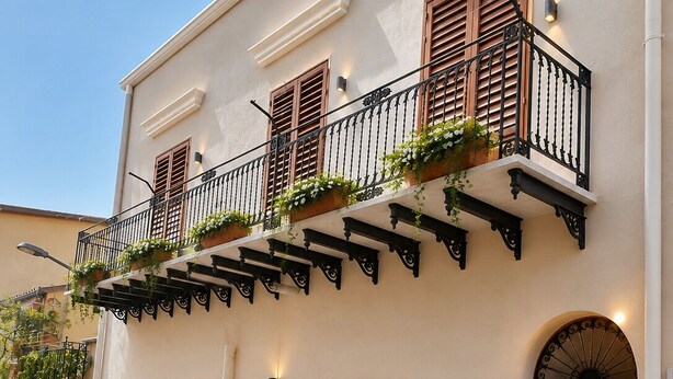 A building with a balcony, potted plants, and a door with a wreath. - Visitsicilia Donn'Anna 1 (Castellammare del Golfo)