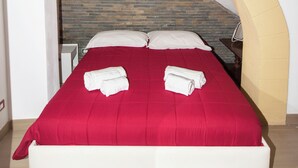 A bed with a red bedspread, white pillows, and two rolled towels. - Visitsicilia Donn'Anna 1 (Castellammare del Golfo)