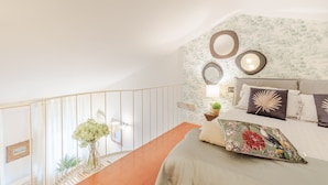 A bedroom with a bed, a nightstand, a wall-mounted mirror, and a staircase. - Cecilia House in Lucca (Lucca)