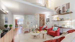A spacious living area with a red sofa, a round coffee table, and a red armchair. There is a staircase leading to an upper level, and a bookshelf with decorative items. - Cecilia House in Lucca (Lucca)